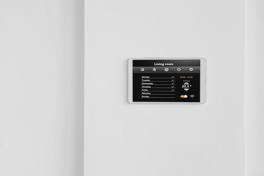 Un écran de contrôle tactile mural gérant la température et le système d'alarme maison dans un intérieur moderne.