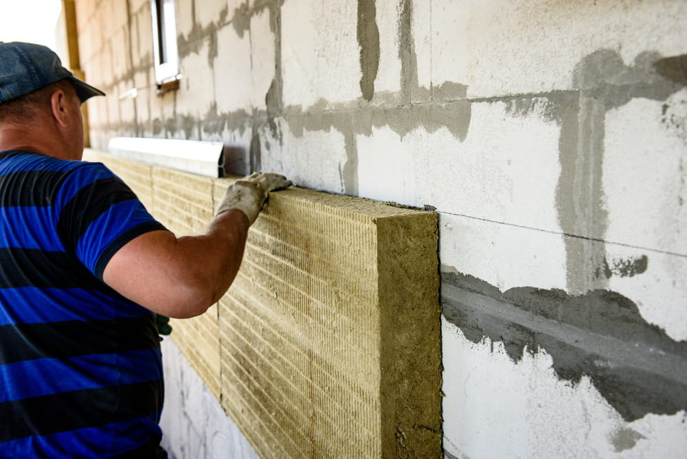 Ouvrier installant un panneau de laine de roche pour une isolation thermique extérieure sur un mur en béton