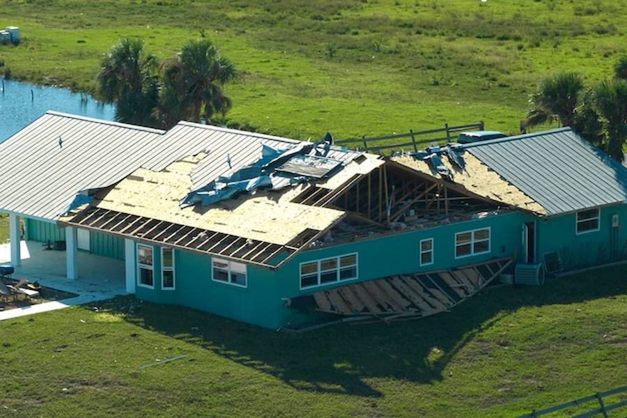 Maison turquoise avec une toiture métallique gravement endommagée par une tempête, illustrant l'importance des normes de construction liées aux attestations re2020.