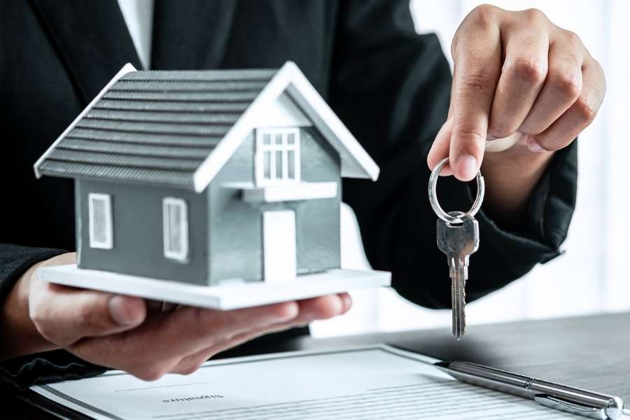 Un professionnel en costume tient une maquette de maison et une clé, symbolisant l'accord final après un compromis de vente.