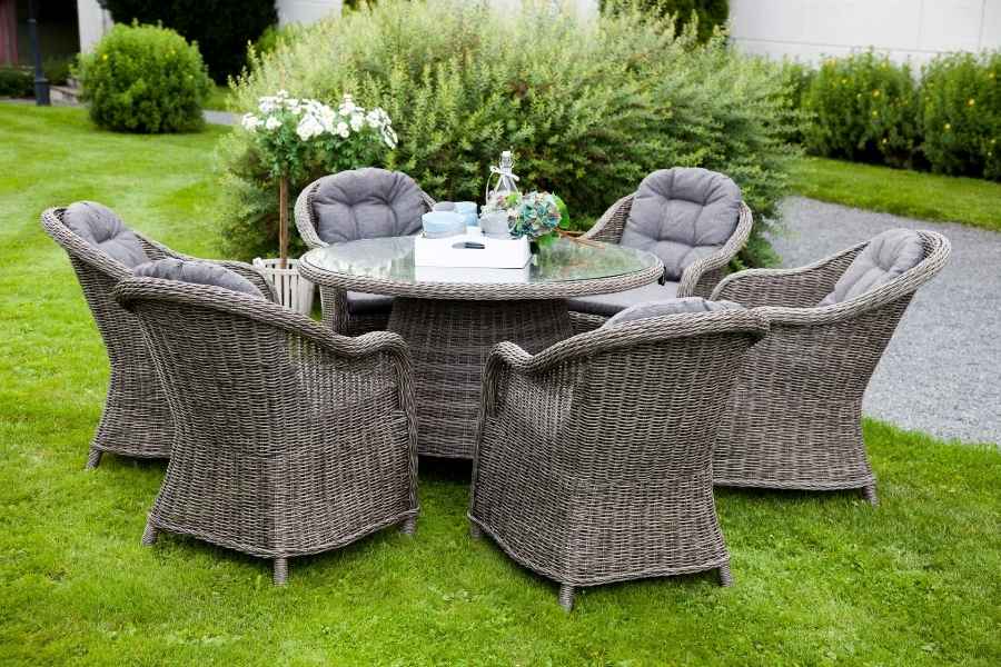 Un ensemble de salle à manger composé de meubles de jardin en résine tressée grise avec des coussins, disposé sur une pelouse.