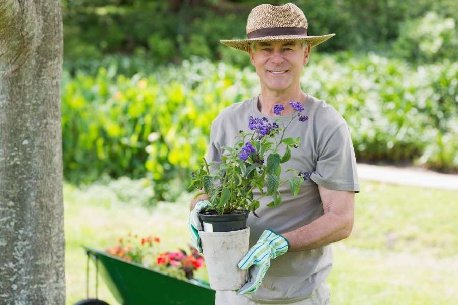 Un jardinier souriant avec un chapeau de paille tient un pot de fleurs.
