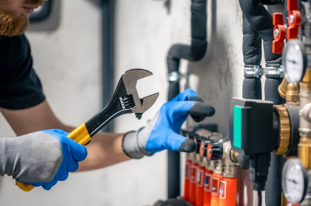 Un technicien utilise une clé à molette pour Comment installer un réducteur de pression en plomberie sur un réseau de tuyauterie.